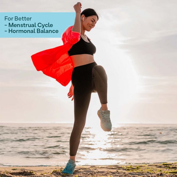 A woman performing a high-kick exercise on the beach with text indicating the product supports better menstrual cycles and hormonal balance.