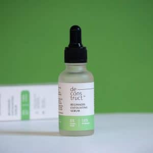 Deconstruct Beginners Exfoliating Serum bottle with 5% Lactic Acid and 1.5% Probiotic, standing against a green background.