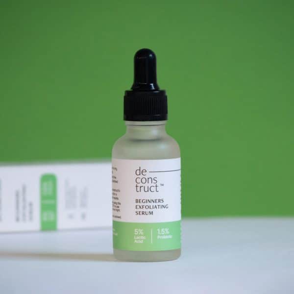 Deconstruct Beginners Exfoliating Serum bottle with 5% Lactic Acid and 1.5% Probiotic, standing against a green background.