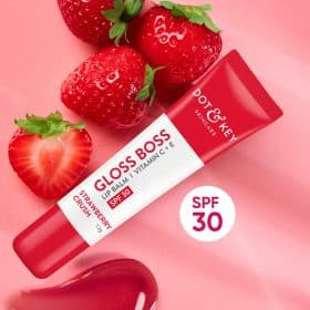 Dot & Key Gloss Boss Lip Balm SPF 30 Strawberry Crush tube with fresh strawberries on a pink background.